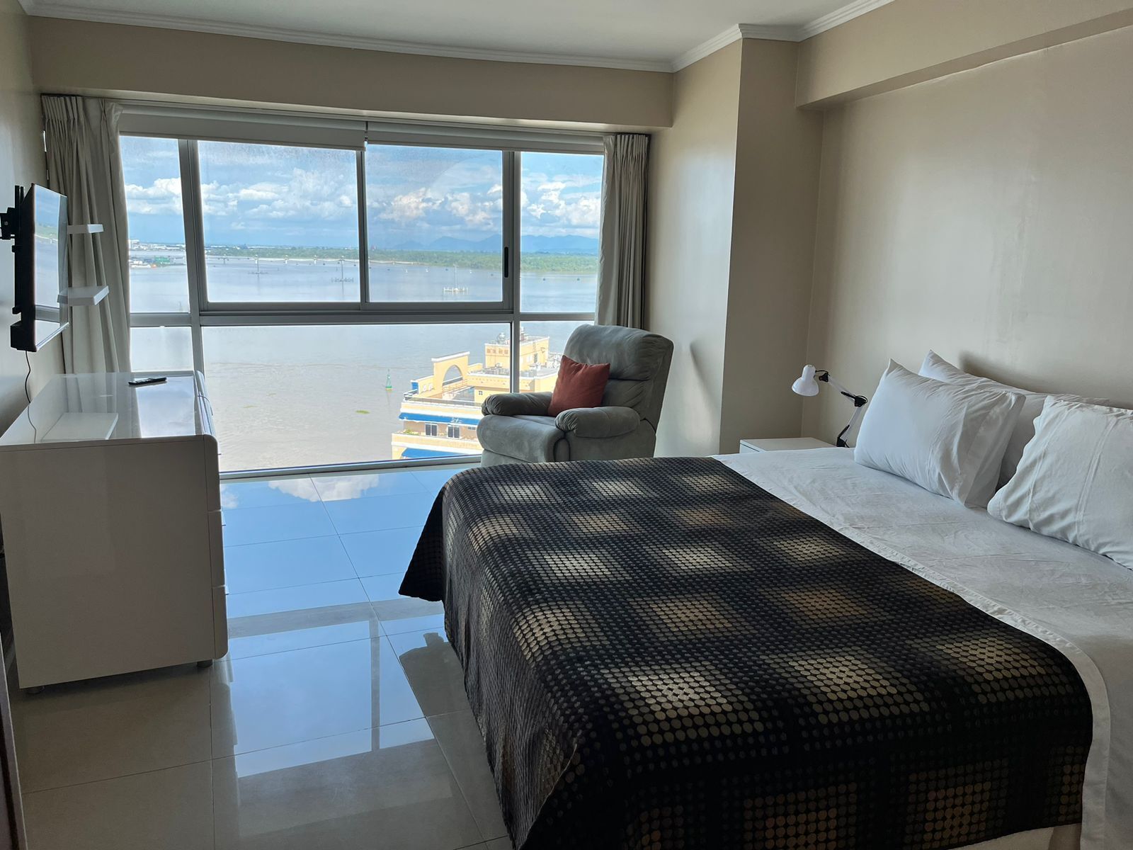 Ein Hotelzimmer mit Bett, Schreibtisch, Stuhl und einem großen Fenster mit Blick auf das Meer und die Stadt.