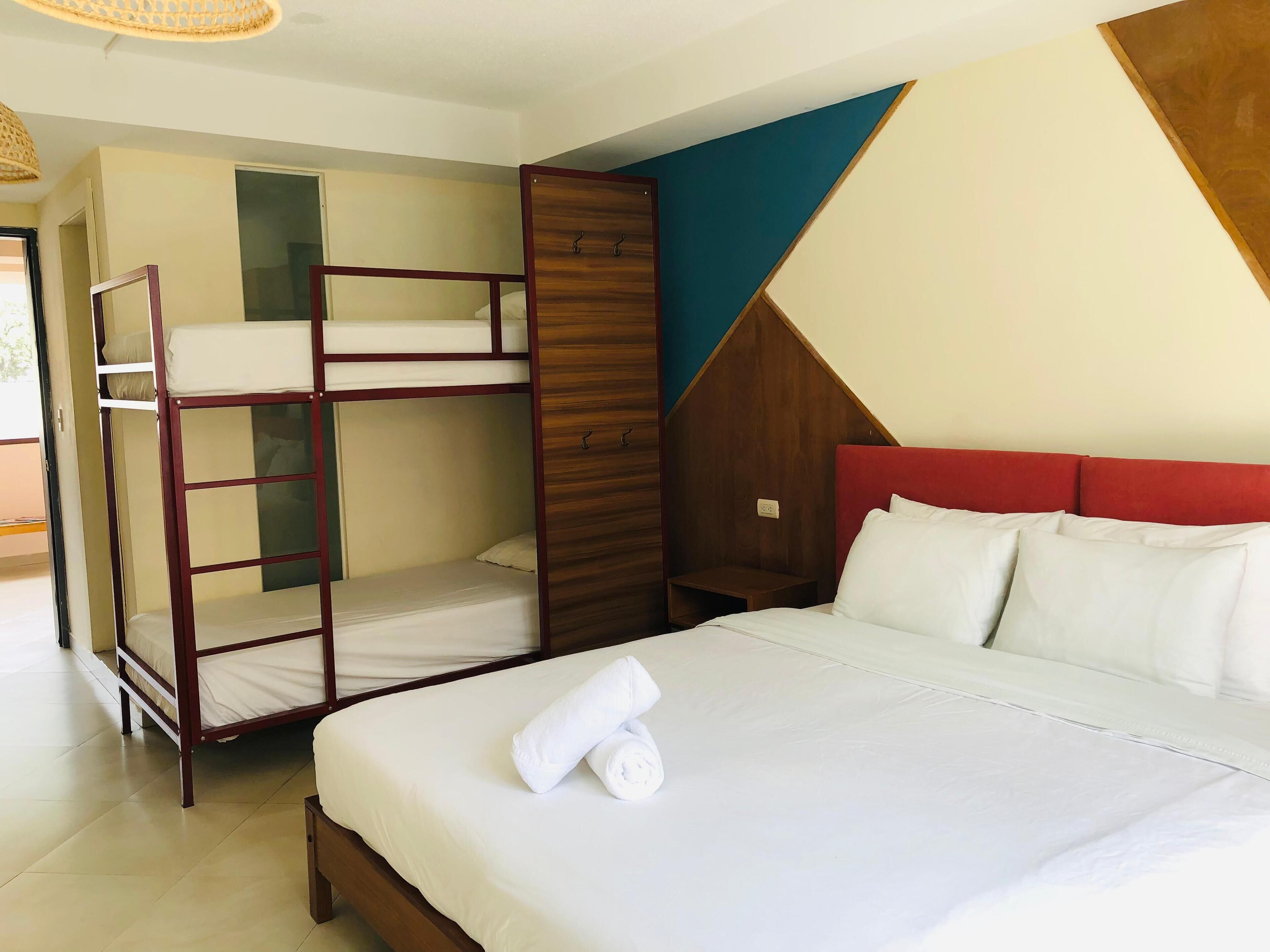 Een hotelkamer met stapelbedden, een houten garderobe, een bed met witte lakens en een wandontwerp met geometrische patronen.