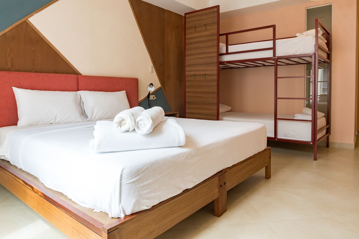 A hotel room with a large bed, a bunk bed, and a desk with a lamp.