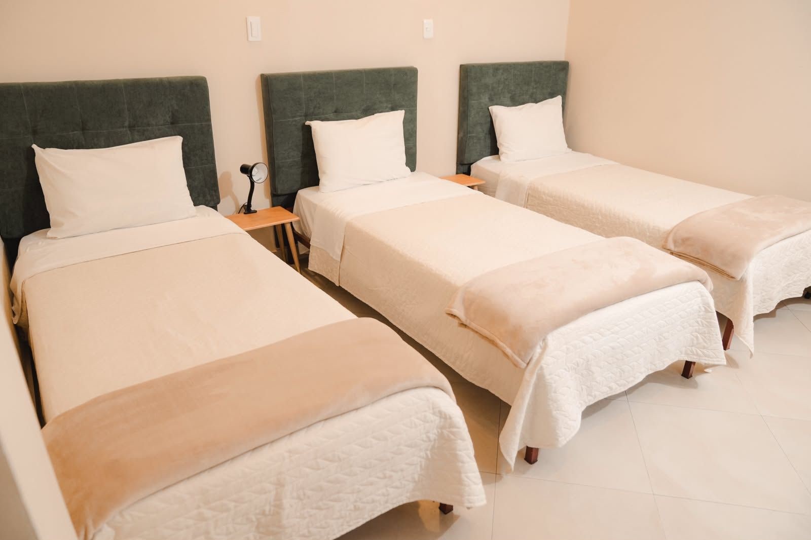 Een hotelkamer met drie eenpersoonsbedden, elk met hoofdeinde en nachtkastje.