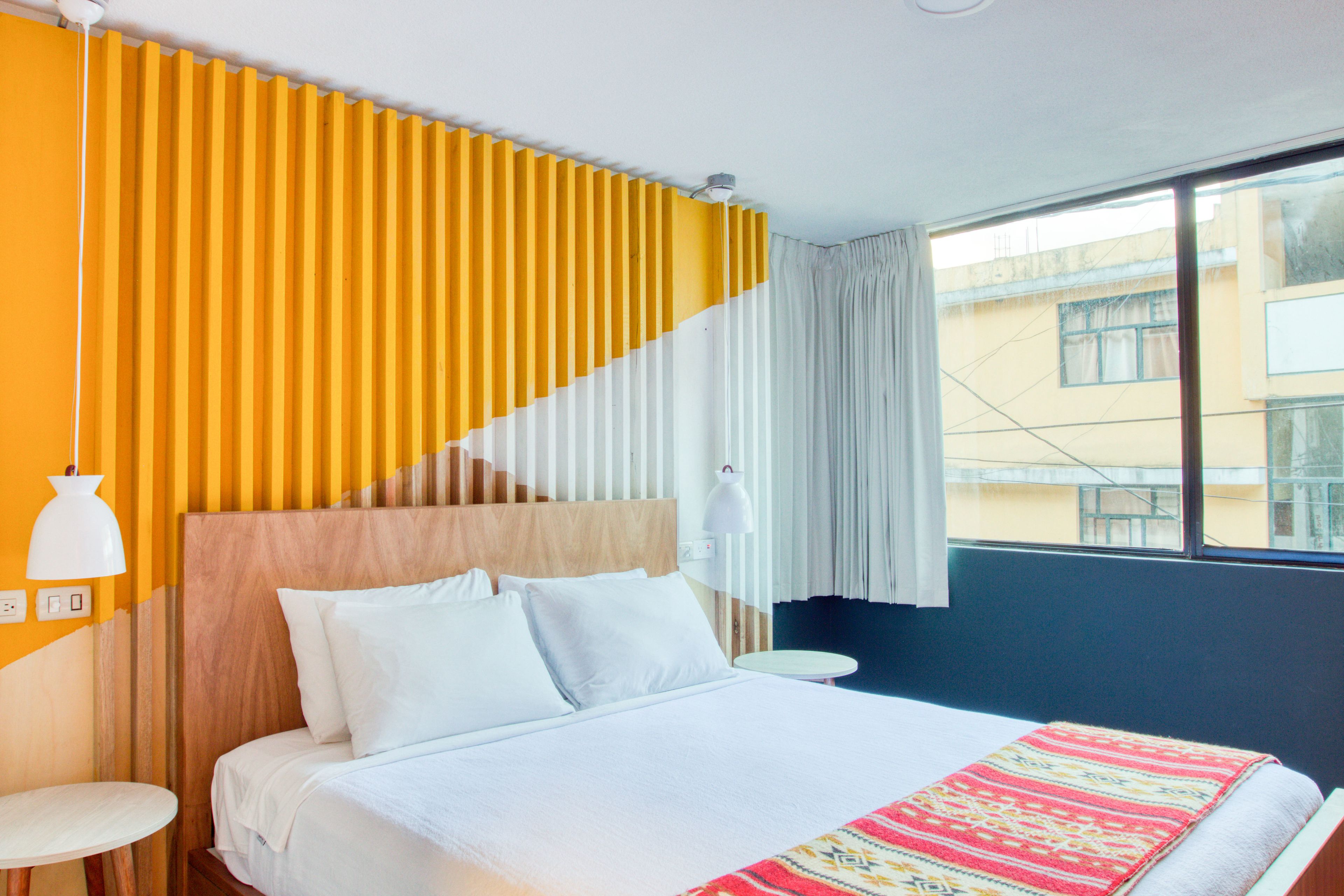 Una habitación de hotel con una cama, una mesa redonda, una lámpara de pared y una ventana con cortinas.