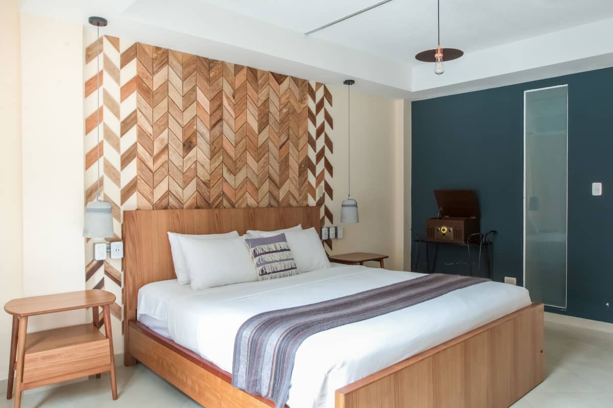 A modern bedroom with a wooden herringbone-patterned headboard, a large bed with white linens, a bedside table, and a radio.