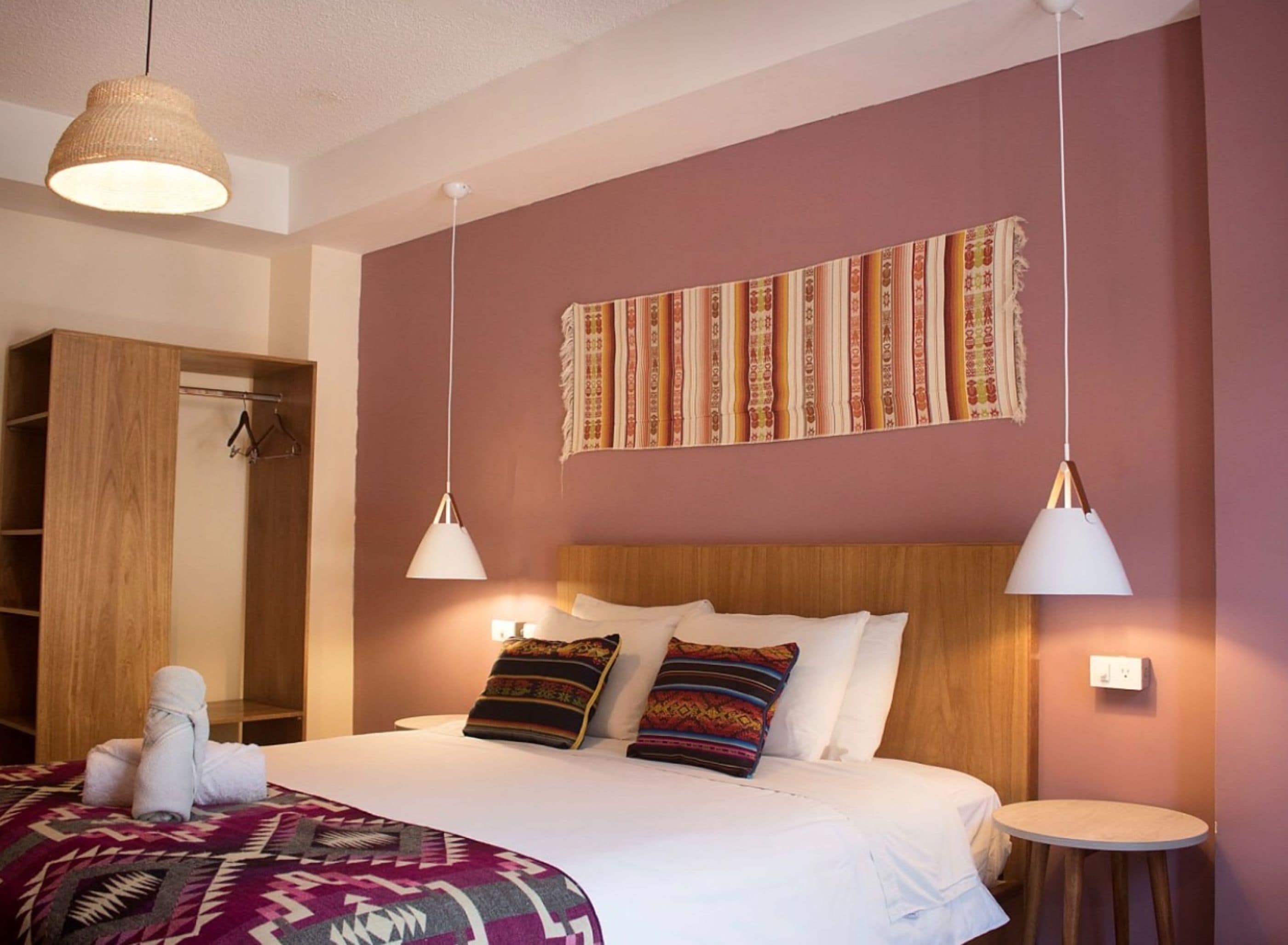 Un dormitorio ordenado con un armario de madera, una cama con almohadones estampados y un tapiz colgado.