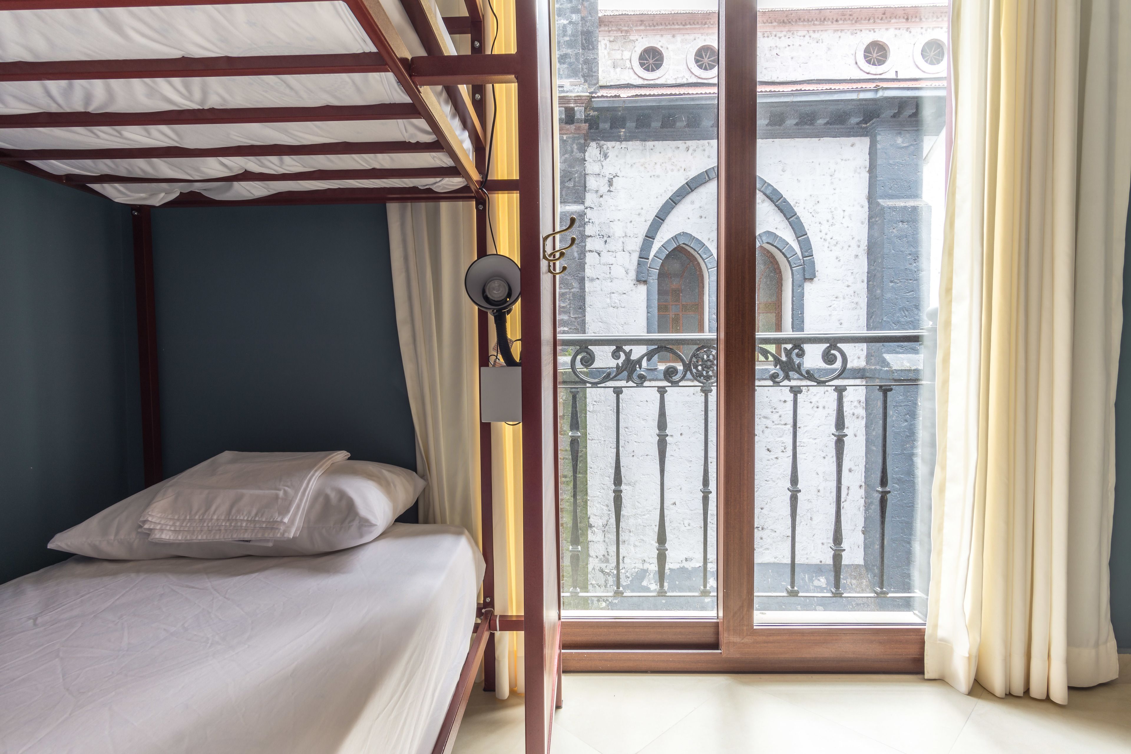 Une chambre à coucher avec un lit, une fenêtre donnant sur un immeuble et un balcon avec une balustrade.