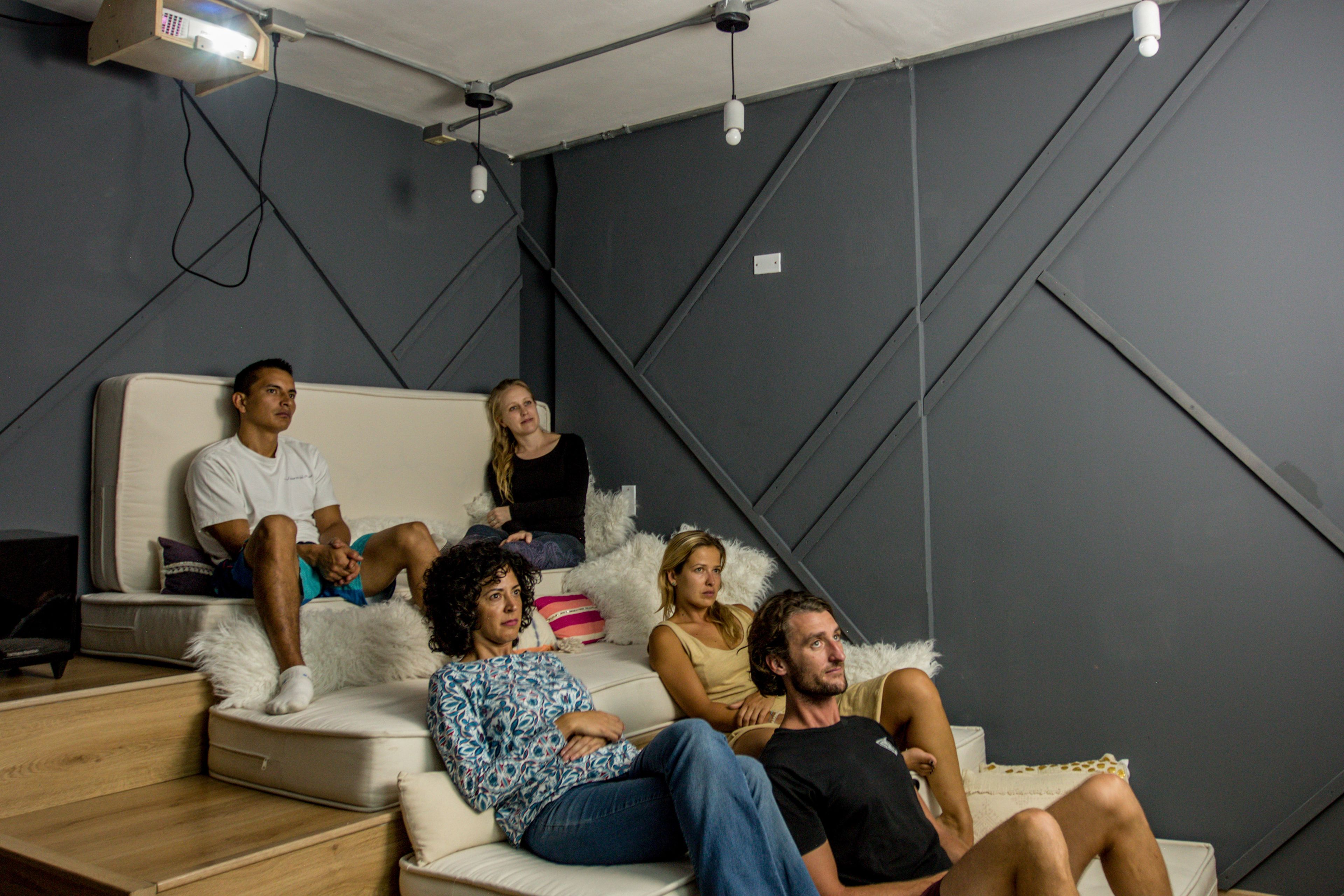 A group of people sitting on a sofa in a room with a modern design, including a geometric wall pattern and a ceiling-mounted projector.