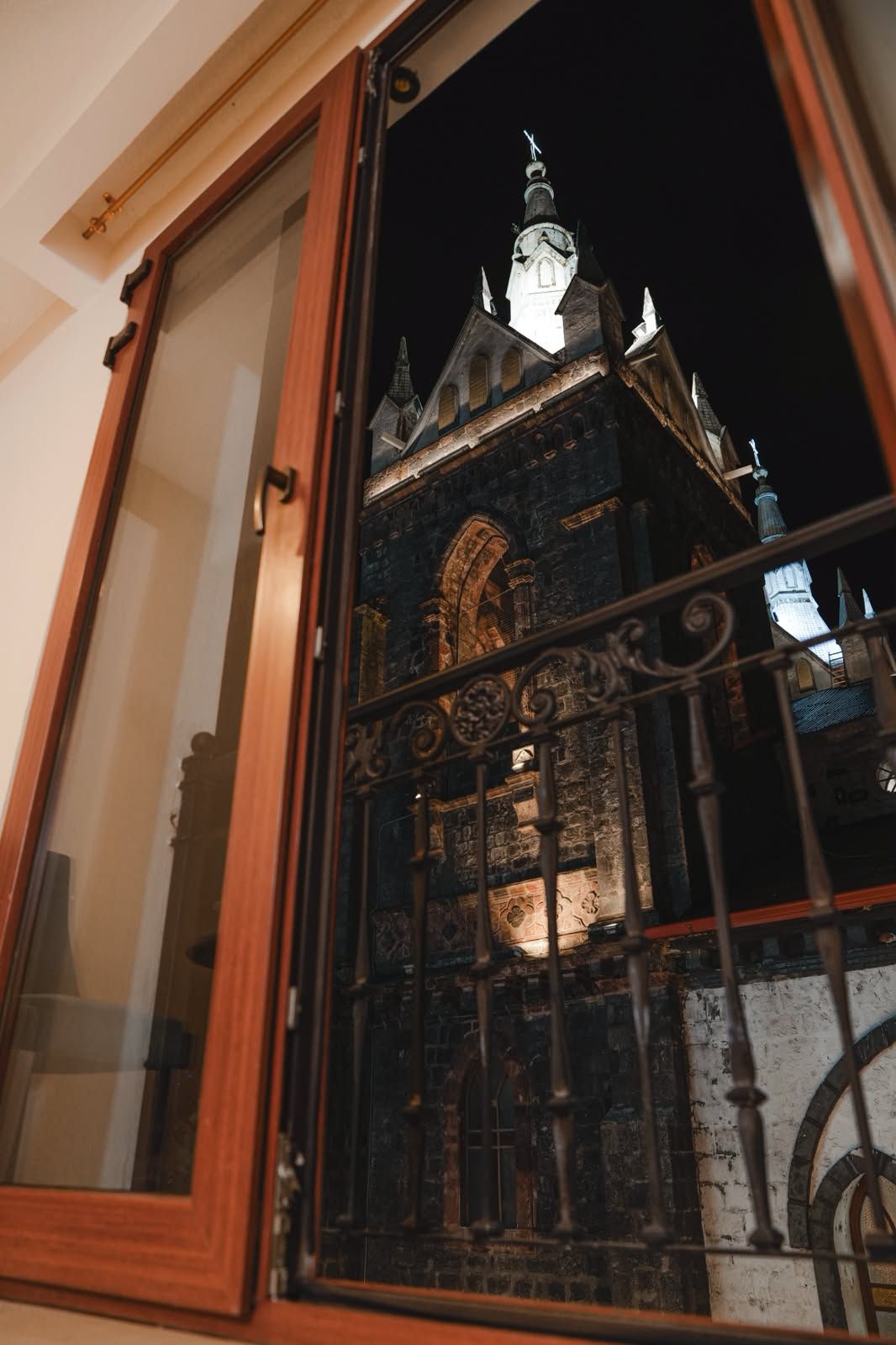 Blick durch ein Fenster mit Metallgitter, das ein historisches Gebäude mit einem markanten Turm und Bogenfenstern zeigt.