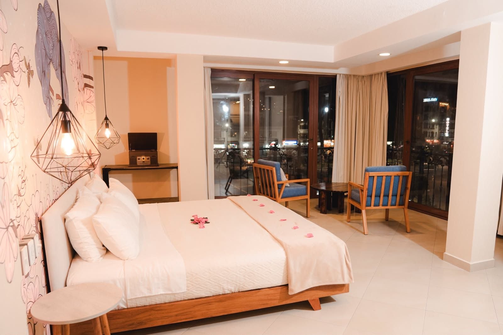 Une chambre d’hôtel avec un lit, un bureau doté d’une radio, un balcon avec des chaises et une vue sur la ville.