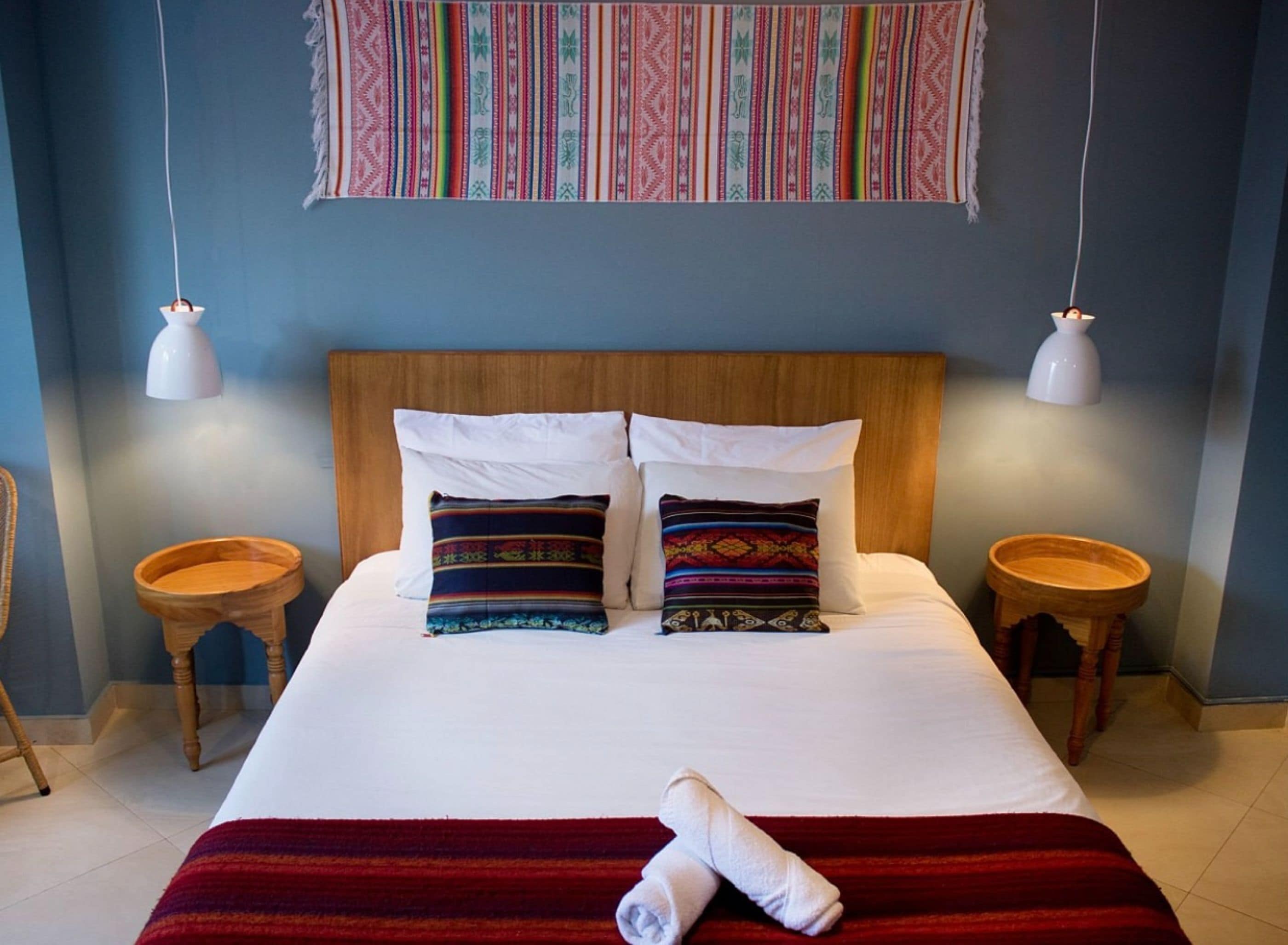 Ein Hotelzimmer mit einem großen Bett, zwei Nachttischen, einem hölzernen Kopfteil und einem farbenfrohen Wandteppich.
