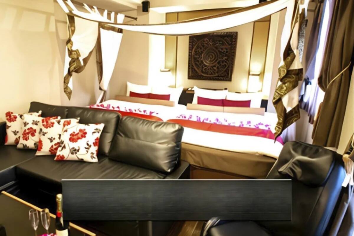 A hotel room with a bed, a sofa, a small table with a bottle and glasses, and a decorative wall piece.