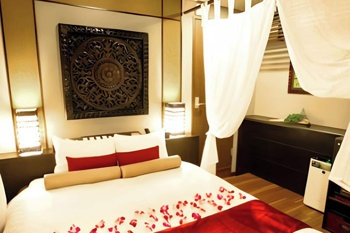A hotel room with a bed, a decorative wall piece, a bedside table, and a nightstand.
