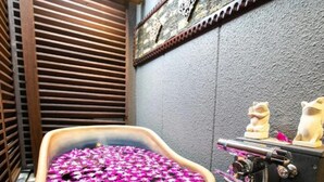 Una bañera llena de flores rosas, listones de madera y un estante con dos estatuillas de gatos.