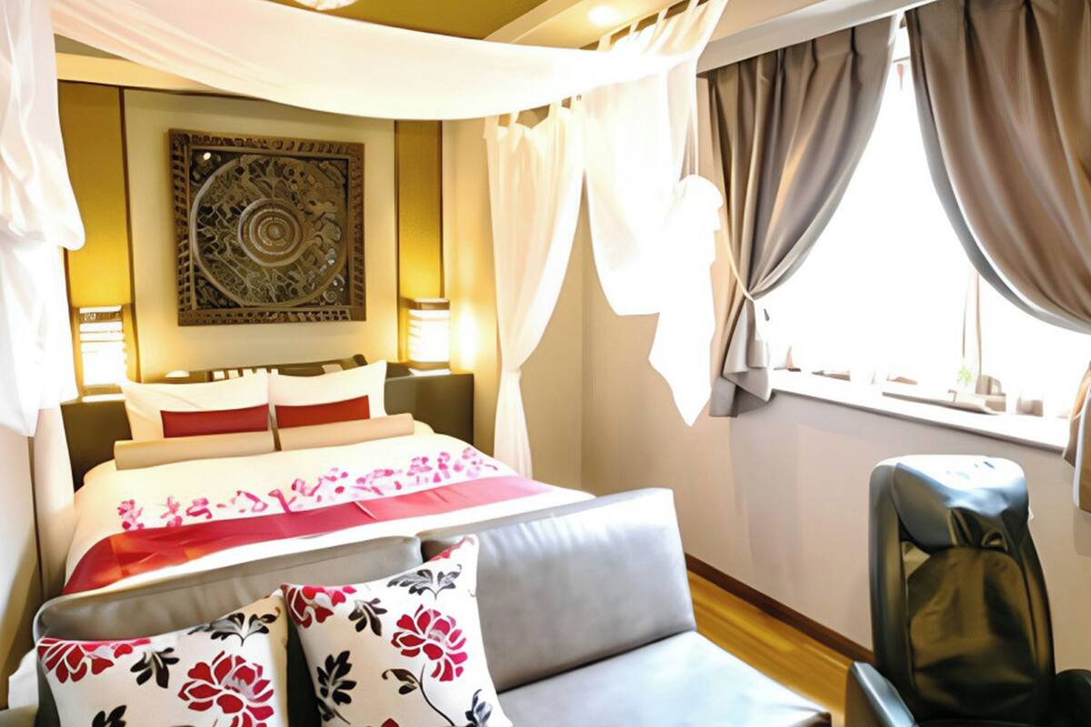 A hotel room with a bed, a sofa, a massage chair, a decorative wall piece, and curtains.