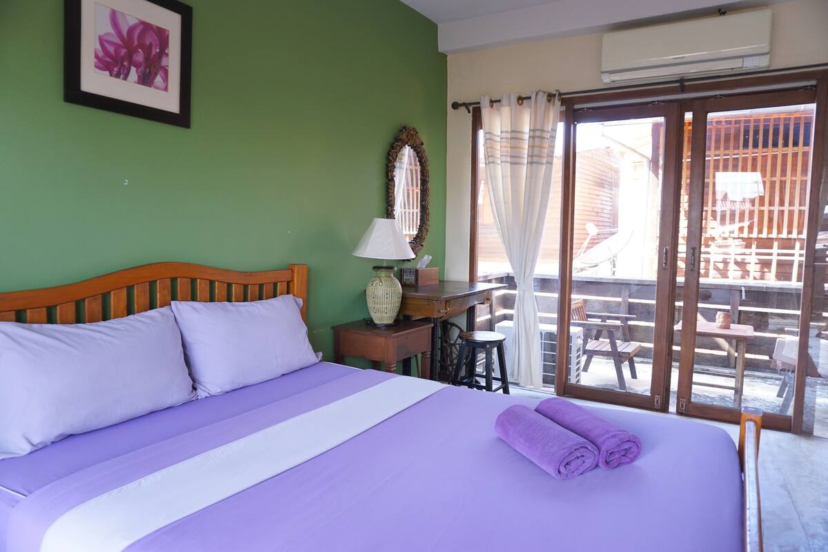 A bedroom with a bed, a nightstand, a lamp, and a view of the outside balcony.