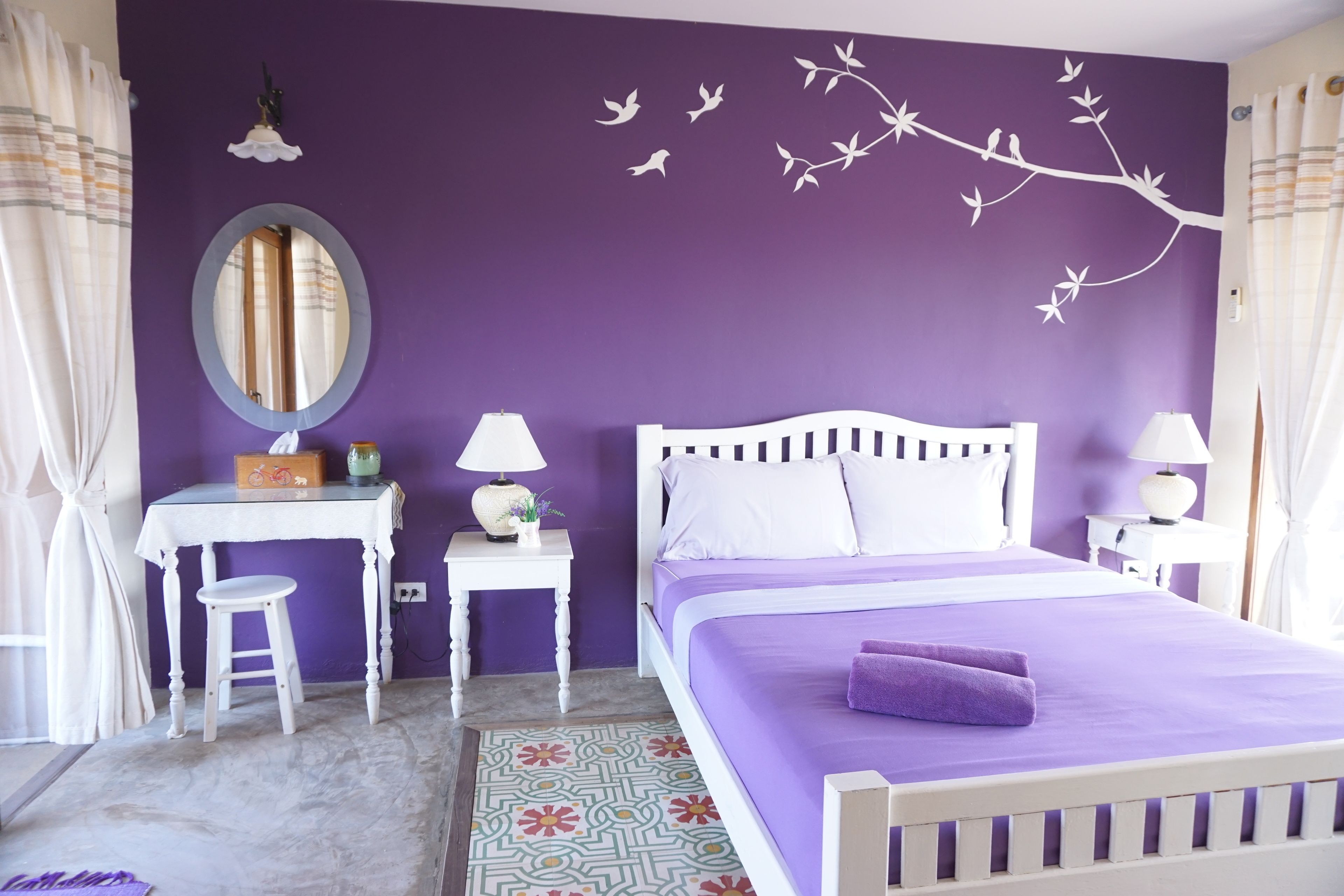 A bedroom with a bed, a desk, a chair, a mirror, and a wall decoration.