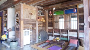 A rustic cabin interior with a wooden floor, a sofa, a dining table, and a large window with a view. - Chiangkhanburi (Chiang Khan)