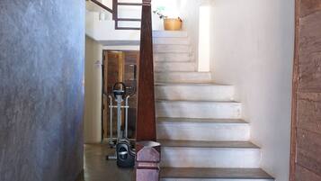 A staircase with a wooden handrail, a concrete wall on the left, and exercise equipment at the bottom.