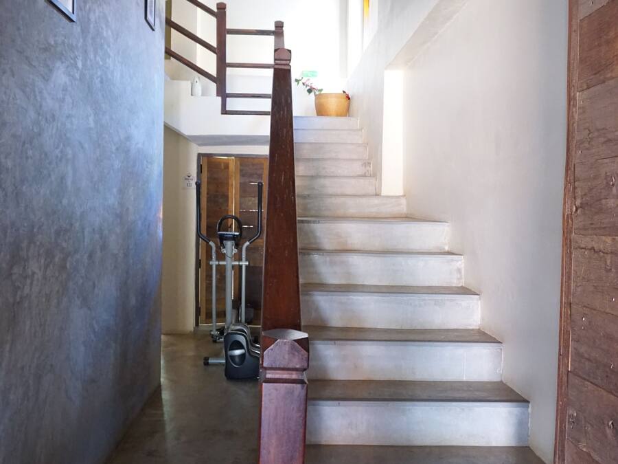 A staircase with a wooden handrail, a concrete wall on the left, and exercise equipment at the bottom.