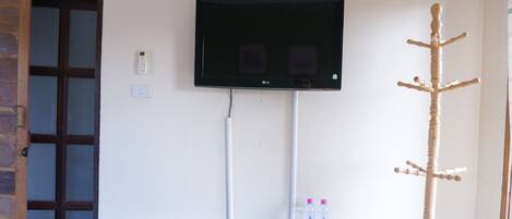 Una habitación con una televisión de pantalla plana montada en la pared, un perchero de madera y una mesita con un control remoto y botellas de agua.