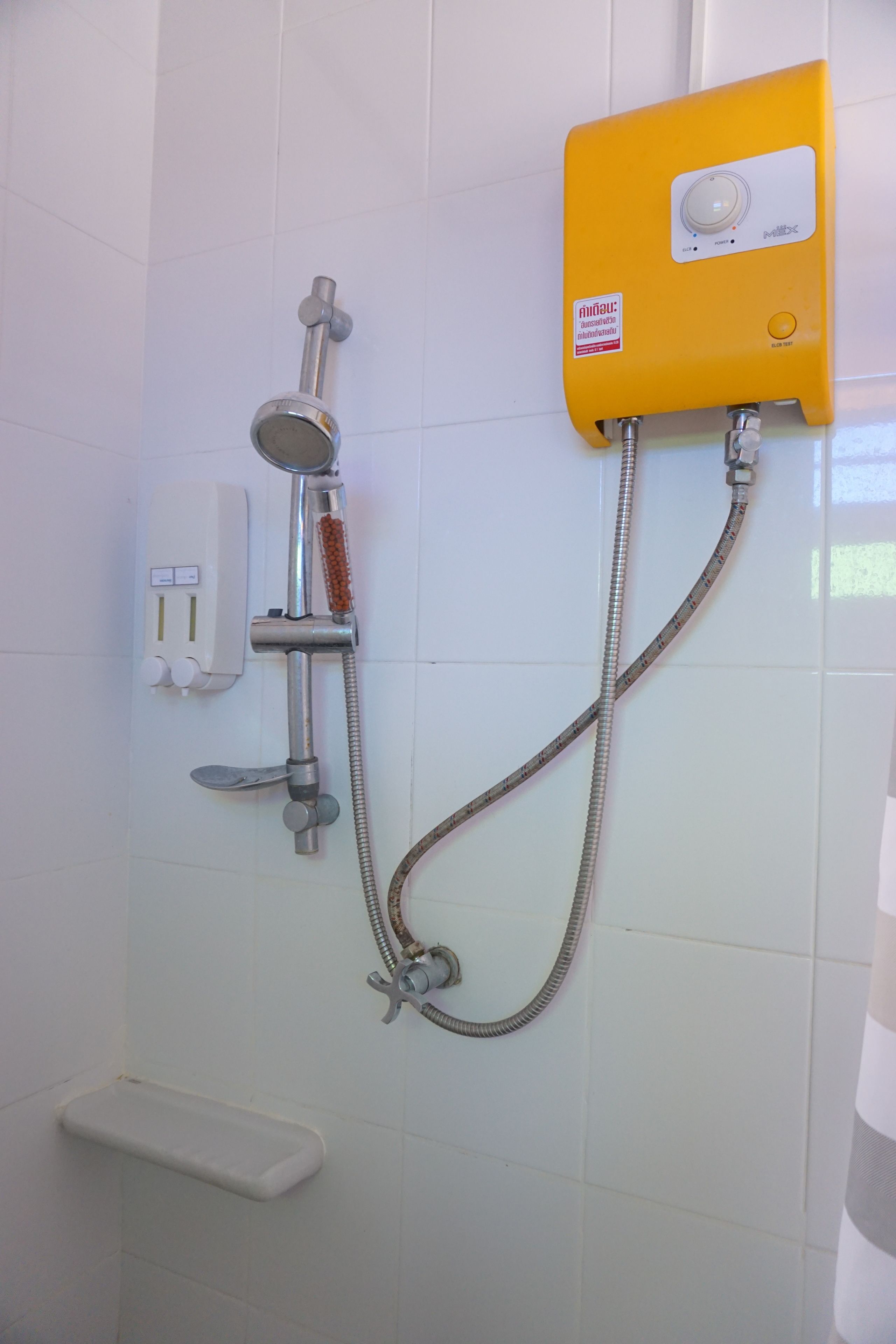 A bathroom with a shower, a yellow water heater, and a soap dispenser.