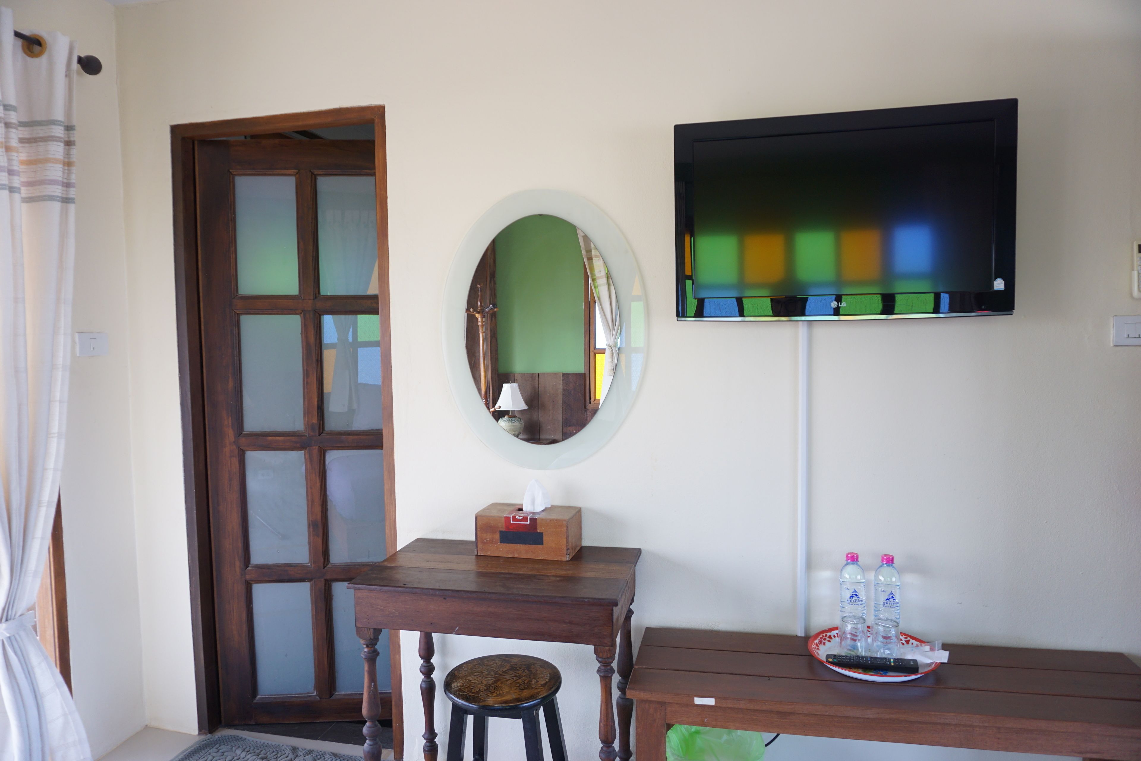 Una stanza con una scrivania in legno, una sedia, una televisione fissata al muro, uno specchio e una porta con pannelli trasparenti opachi.