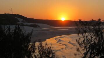 A sunset over a river with a sandy bank and sparse vegetation.