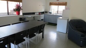 Een functionele keuken met een eettafel, stoelen, een magnetron, een koelkast en een plafondventilator.