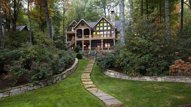 A two-story log cabin with a stone staircase leading to a wooden deck.