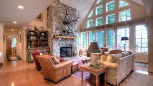 A spacious living room with a stone fireplace, leather furniture, and a large window with curtains.