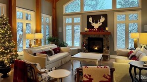A cozy living room with a fireplace, large windows, and a Christmas tree.