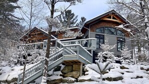 A two-story log cabin with a stone foundation, a wooden deck, and a staircase leading to the upper level.