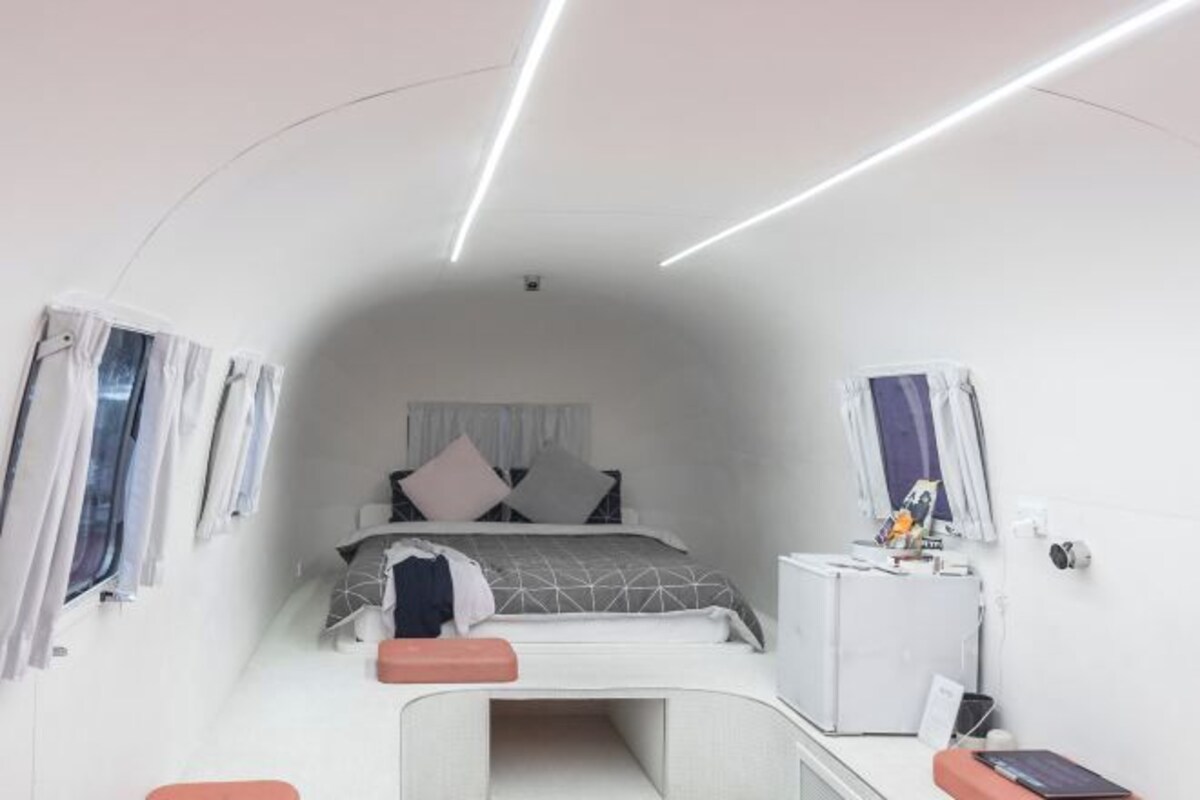 A modern, compact bedroom with a bed, bedside table, and a small desk area.