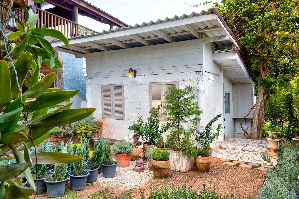 A white building with a tiled roof and a garden with various potted plants.