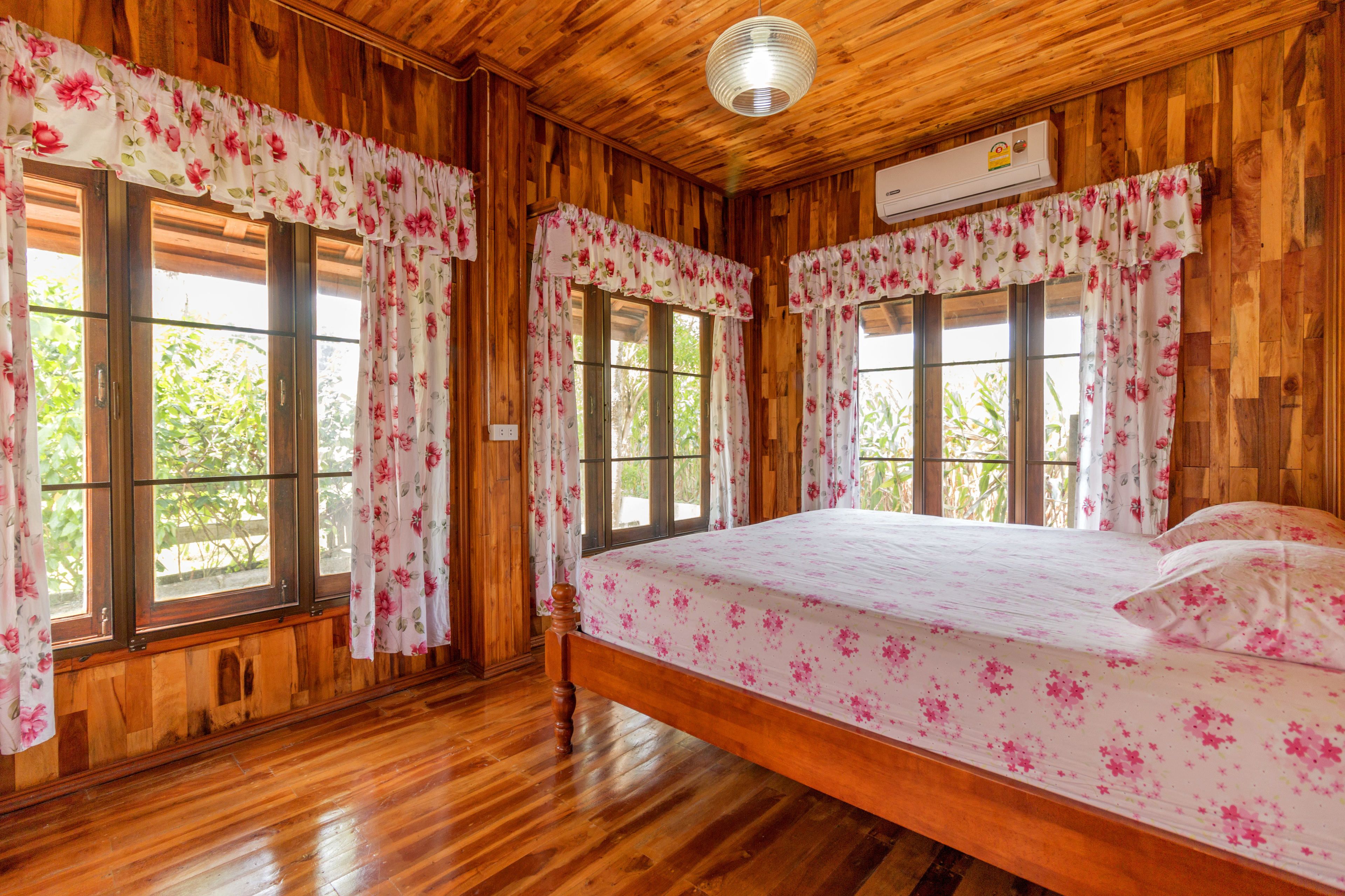 A wooden room with a bed, large windows, and floral curtains.