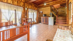 A wooden cabin interior with a dining area, a kitchen, and a staircase. - Rosemary House (Pak Chong)