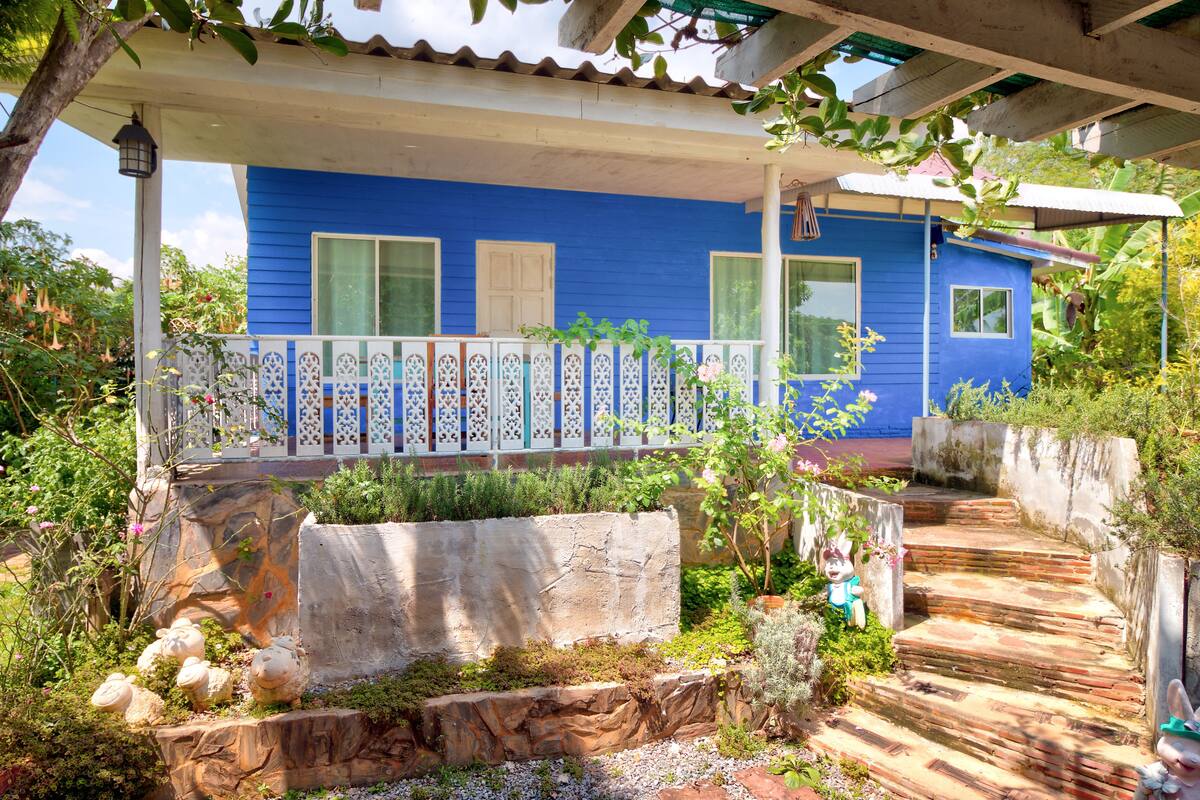 A blue house with a porch, a stone retaining wall, and a wooden staircase.