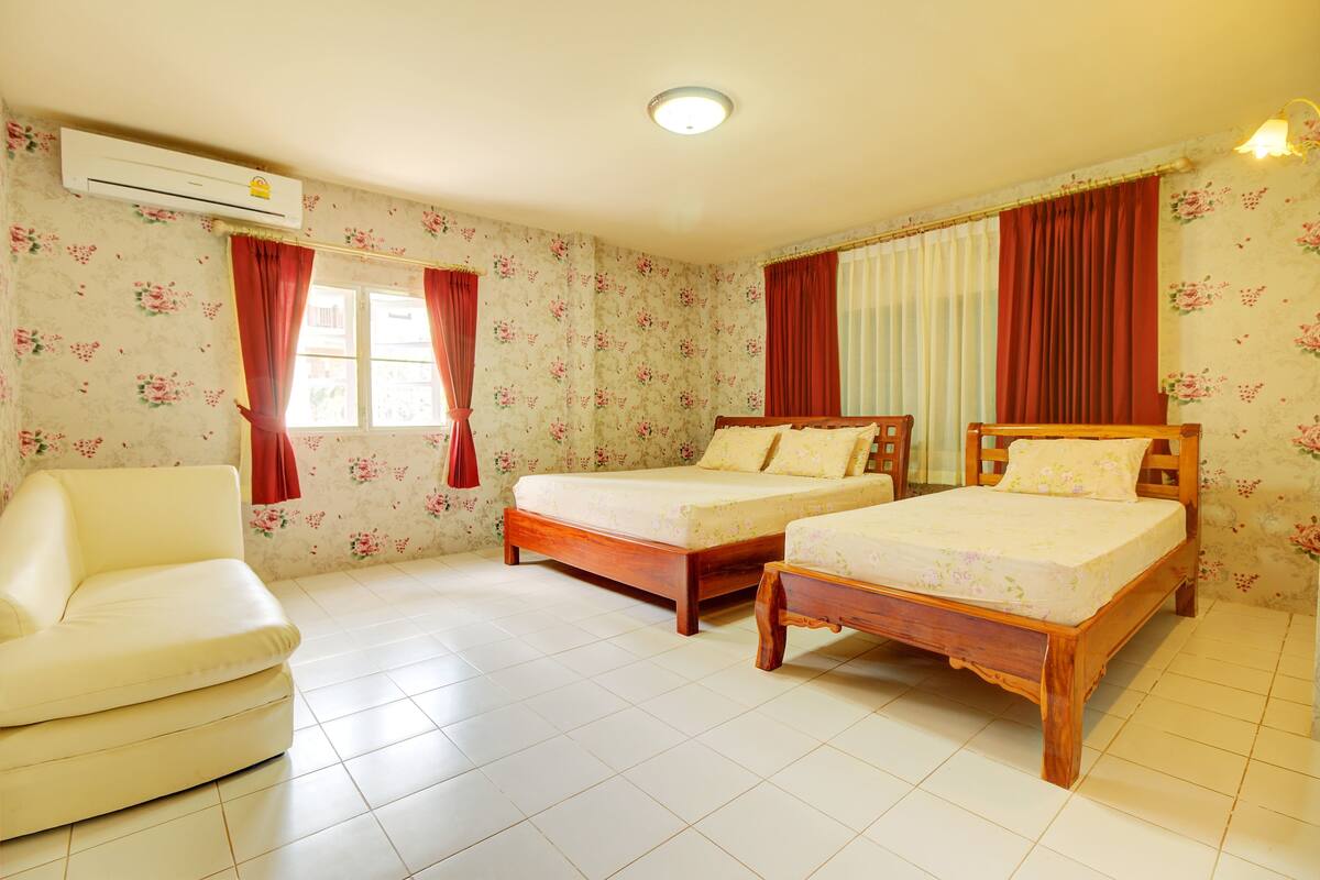 A room with two wooden beds, a white sofa, and a window with red curtains.