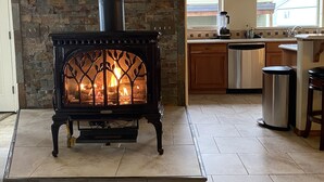 Una chimenea de piedra con un conducto negro, una cocina con lavavajillas y un ventanal con vista a una casa.
