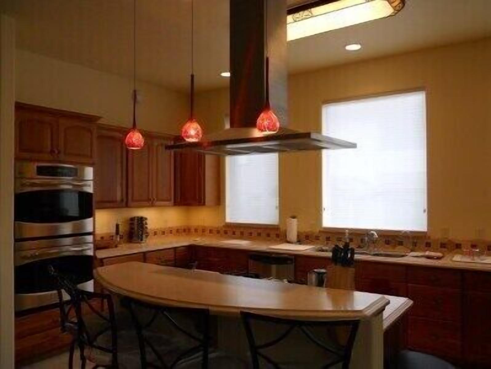 A modern kitchen with wooden cabinets, a stainless steel oven, a central island with bar stools, and pendant lighting.