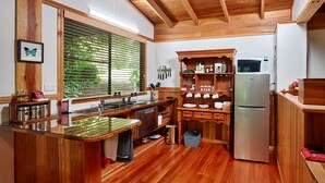 A kitchen with wooden cabinetry, a stainless steel refrigerator, and a window with blinds. - Sharlynn by the River (Malanda)
