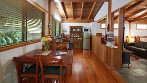 A spacious kitchen with wooden beams, a dining area with a table and chairs, and a living area with a couch. - Sharlynn by the River (Malanda)