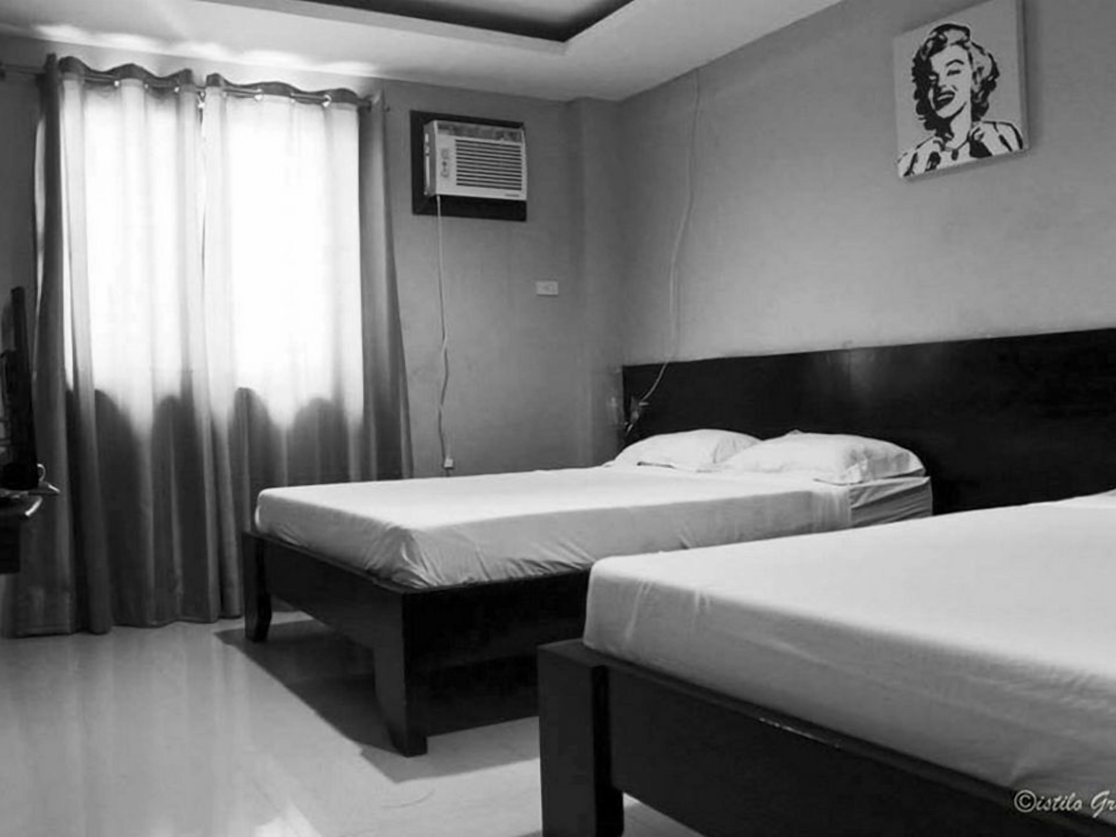 Quarto de hotel com duas camas de solteiro, televisão e janela com cortinas.