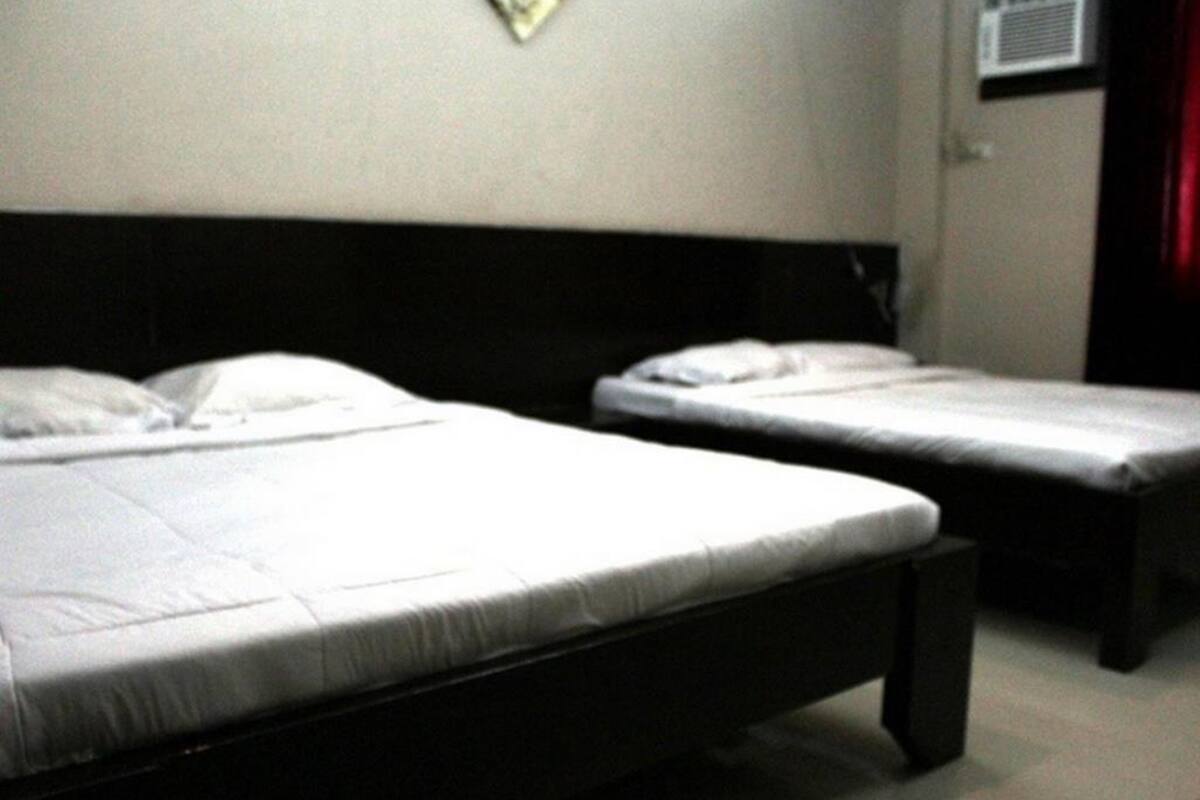 Una habitación con dos camas individuales, un cabecero negro, una pared blanca y un equipo de aire acondicionado pequeño.