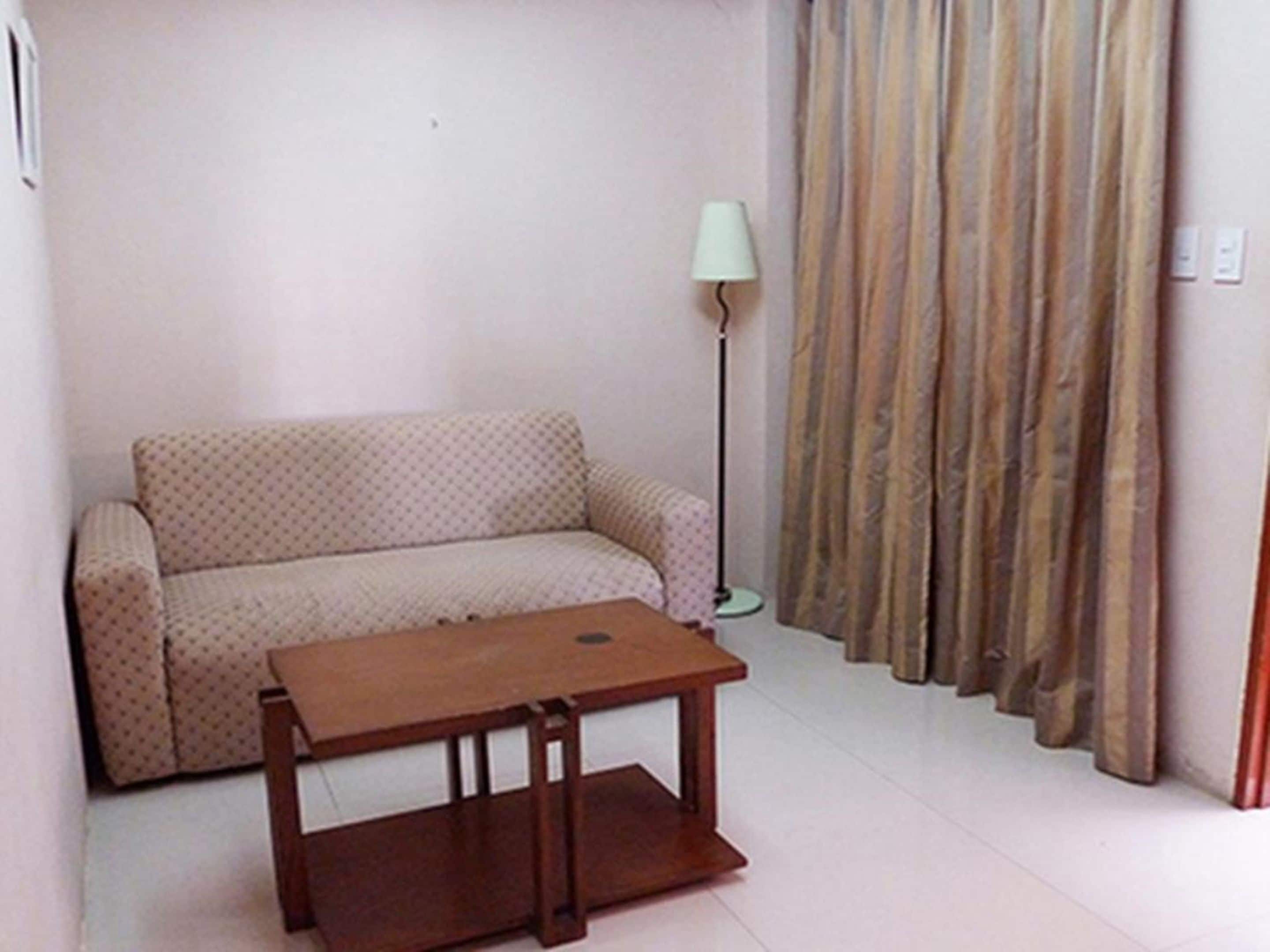 A living room with a sofa, a small wooden table, a floor lamp, and curtains.