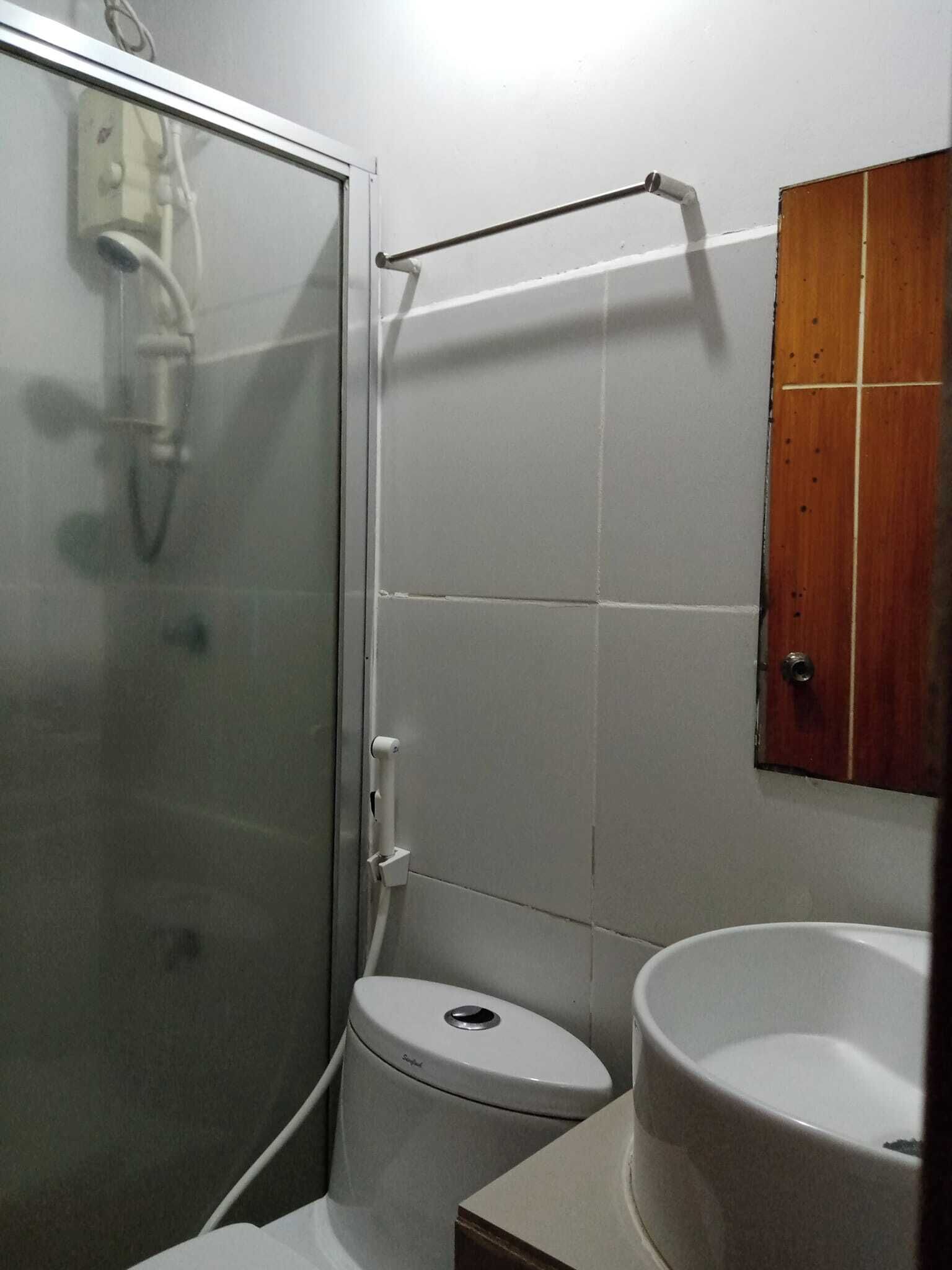 A bathroom with a glass shower enclosure, a white toilet, and a wooden cabinet above the sink.