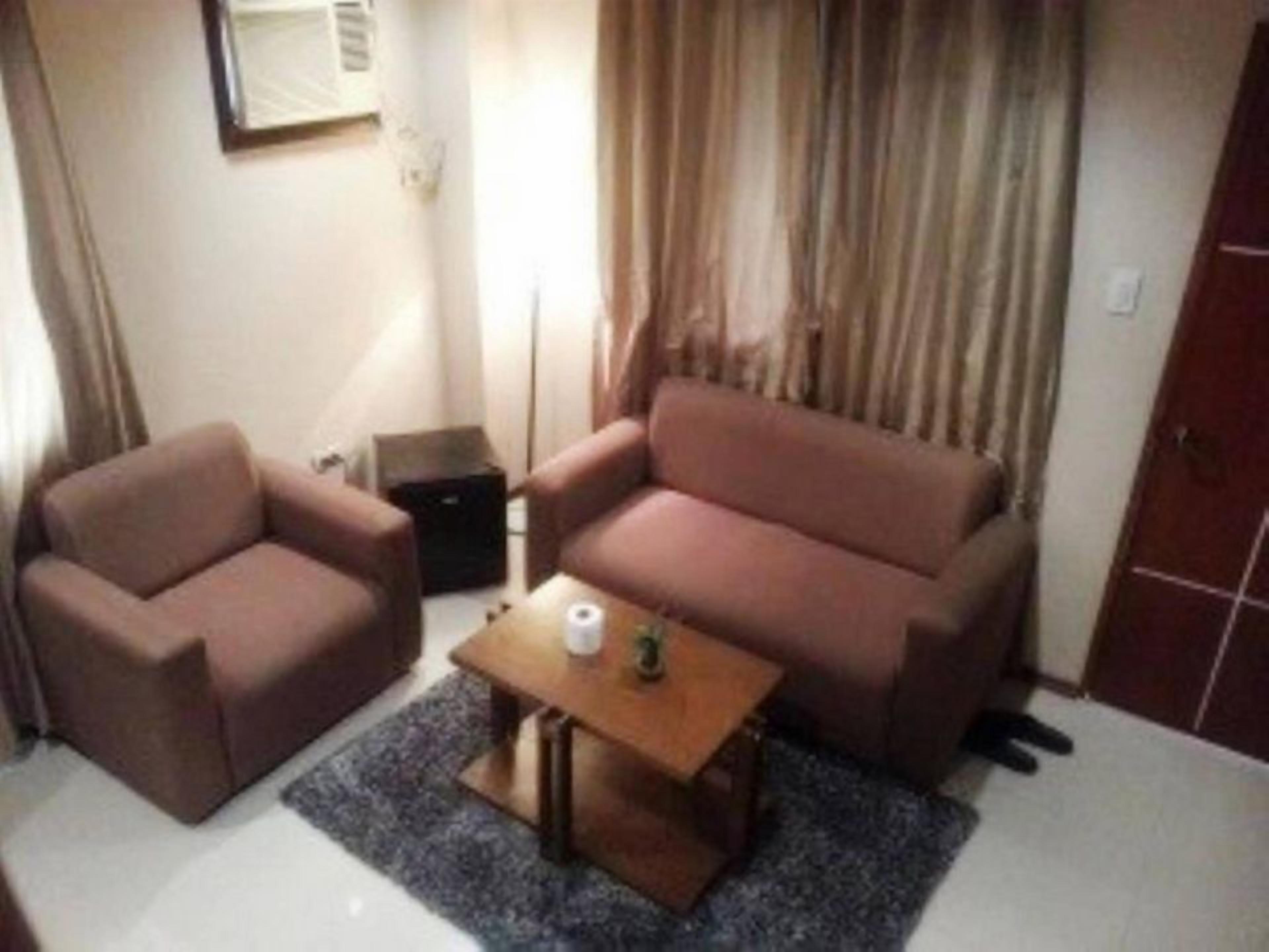 A small living area with a sofa and armchair, a small table, and a window with curtains.