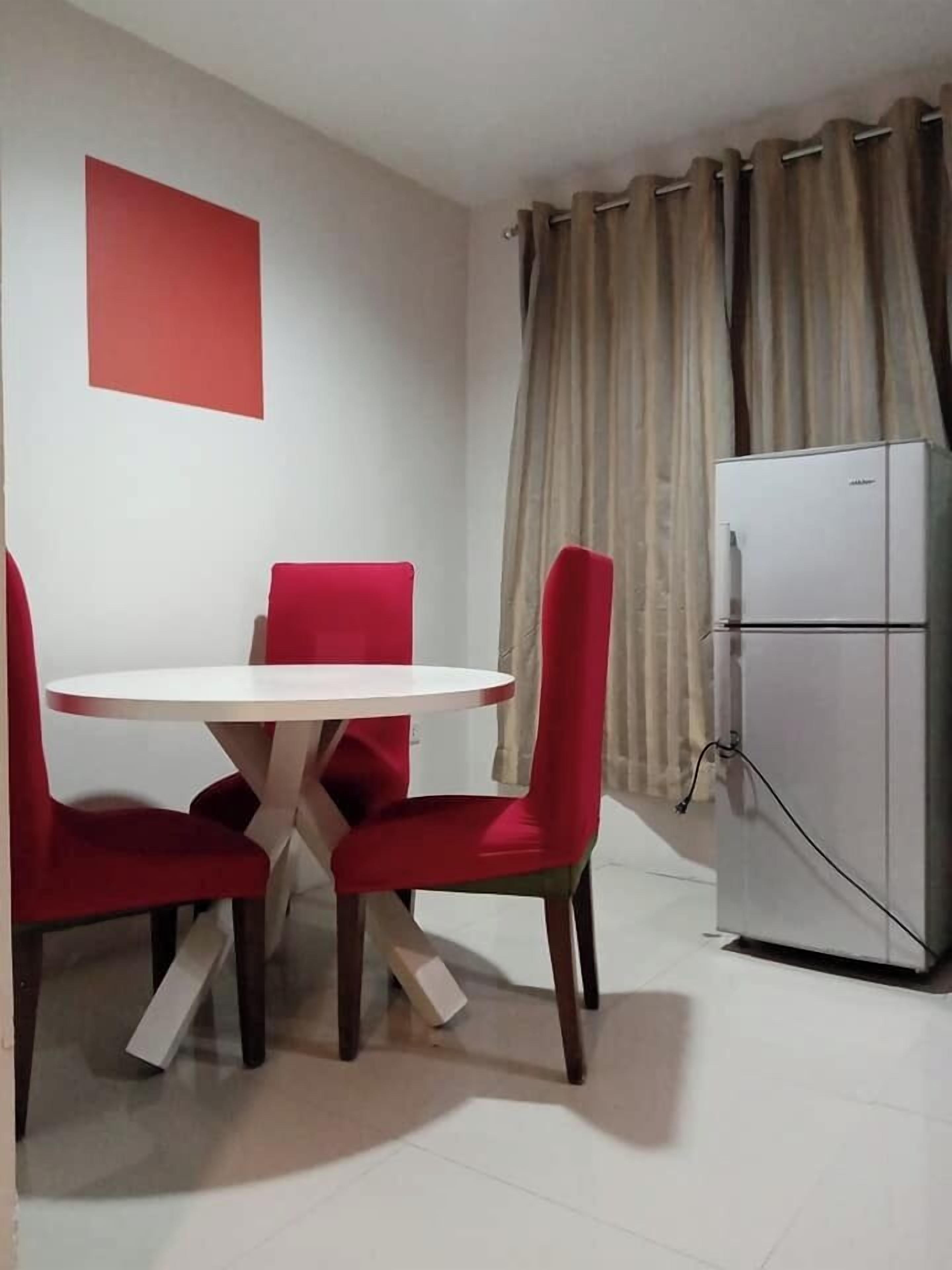 Un'area pranzo con un tavolo rotondo bianco e sedie rosse, un frigorifero bianco e tende beige.