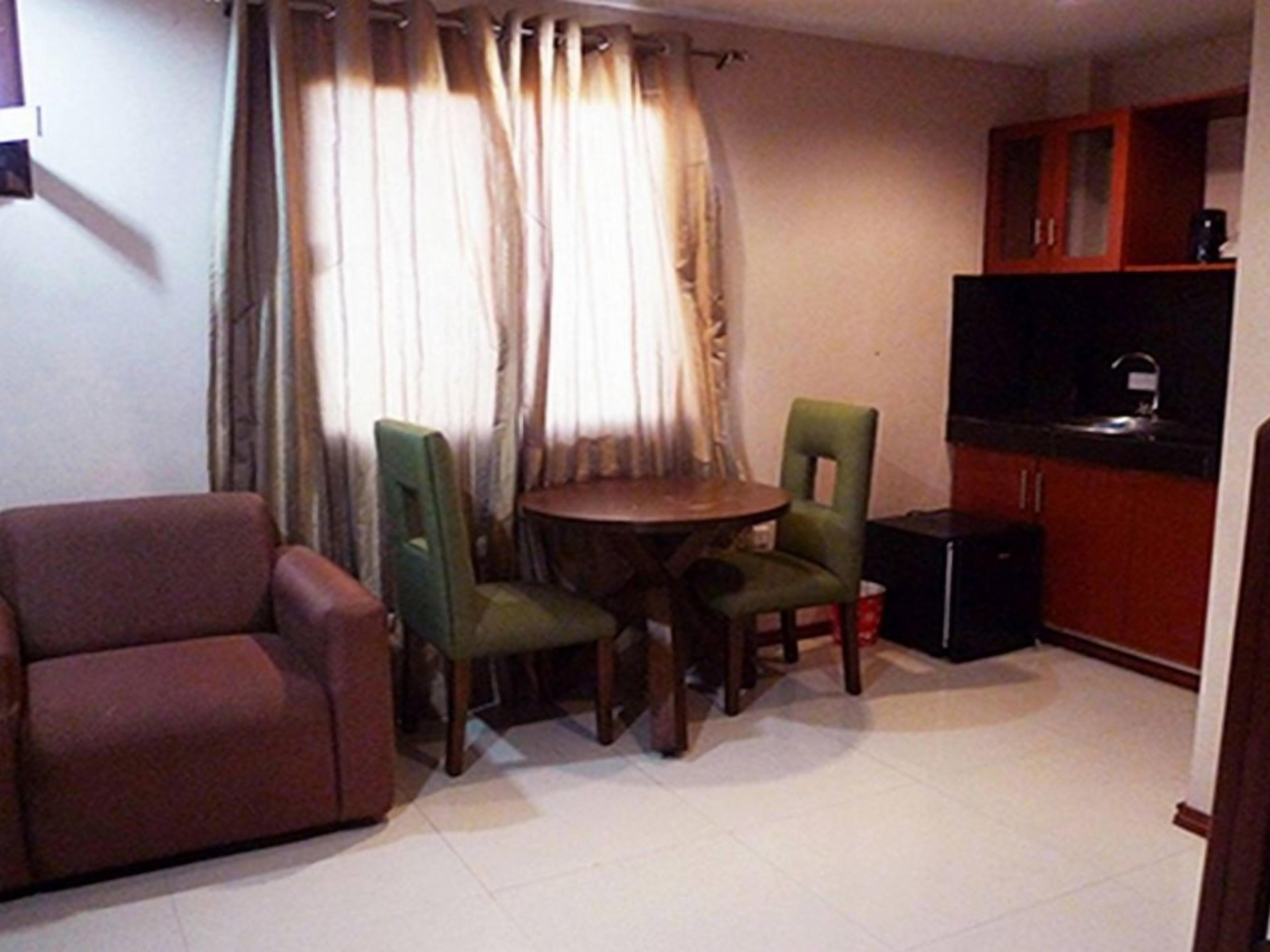 Un espacio habitable compacto con un sofá, dos sillones, una pequeña mesa redonda, un televisor y una zona de kitchenette.