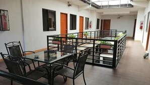 Un espace intérieur spacieux avec une table et des chaises en verre, un balcon agrémenté de plantes en pot et un extincteur fixé au mur.