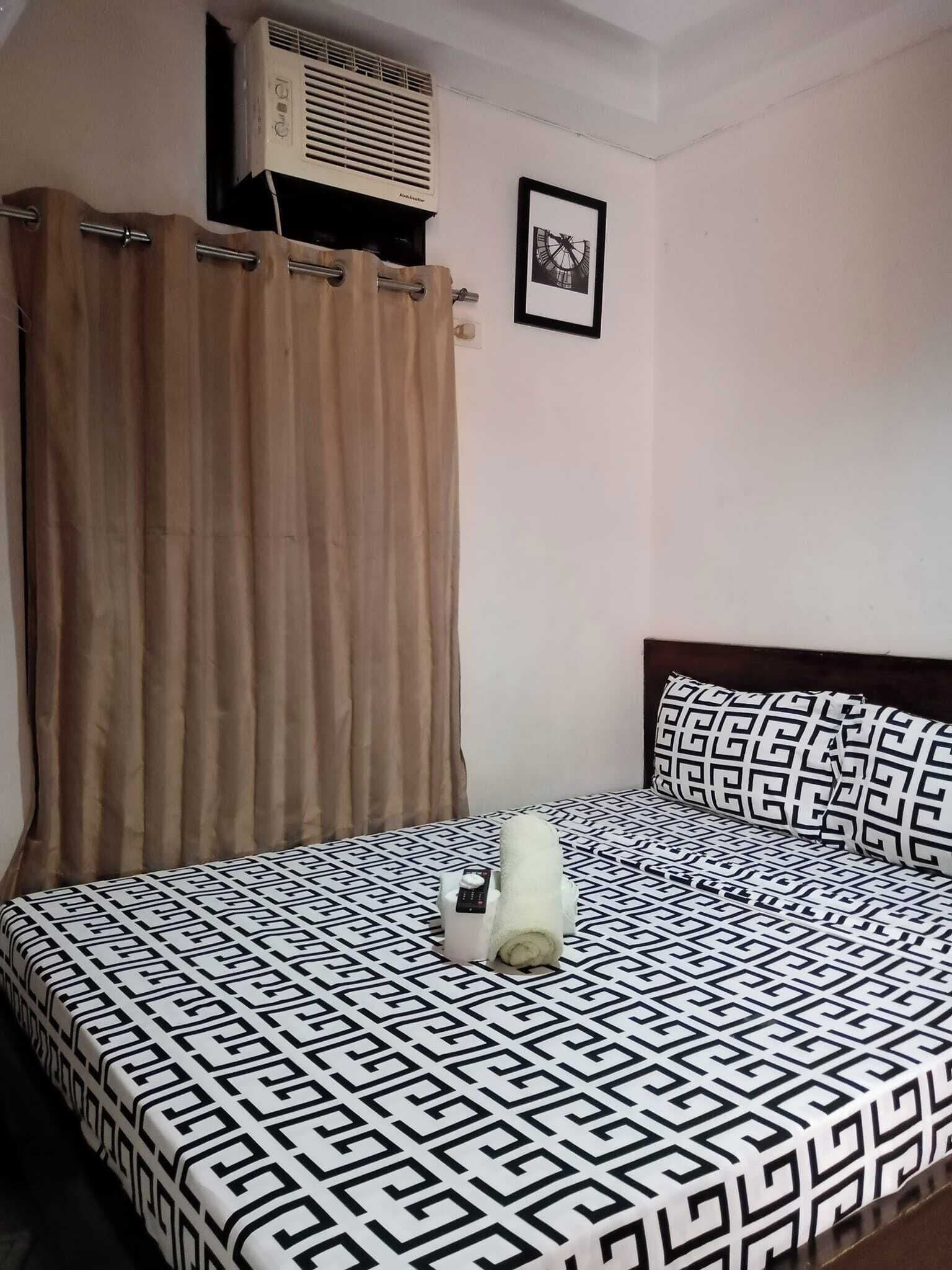 Una cama con una colcha estampada, una almohada y una toalla enrollada.