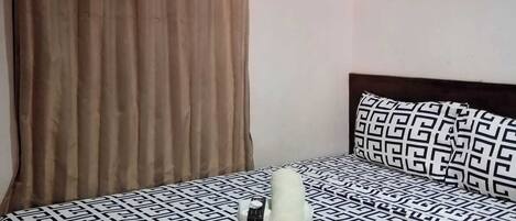 Una cama con una colcha estampada, una almohada y una toalla enrollada.